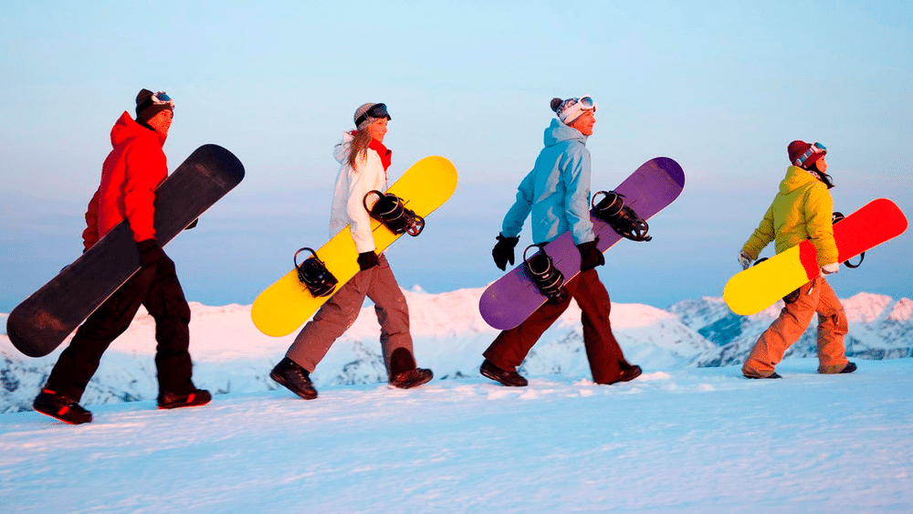 Snowboarders walking on snow carrying snowboards.  Outdoor safety and wilderness risk management are considerations for frontcountry and backcountry snow sports.